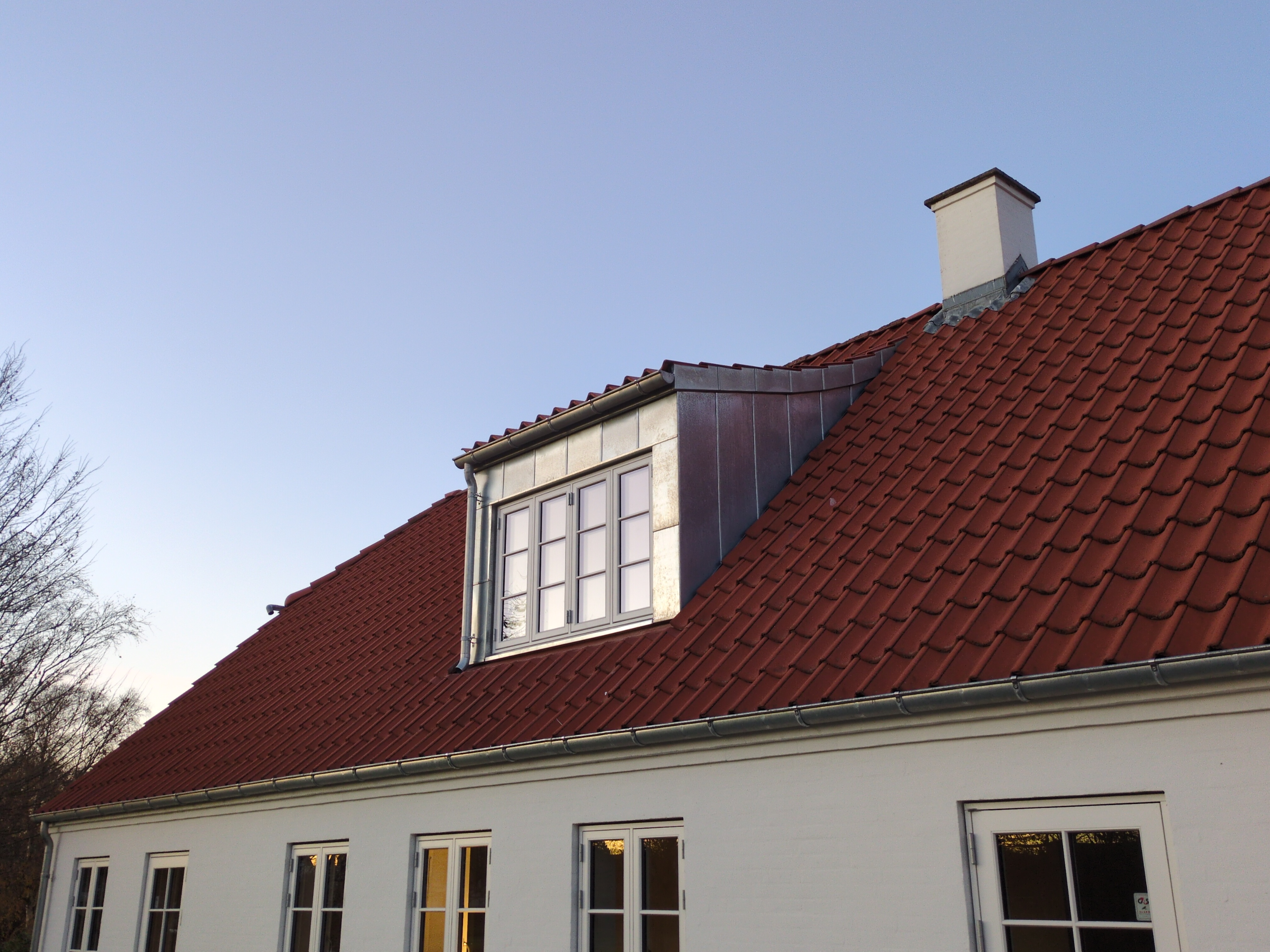 Hvidt hus med ny zinkbeklædt taskekvist og rødt tegltag ved aftenlys